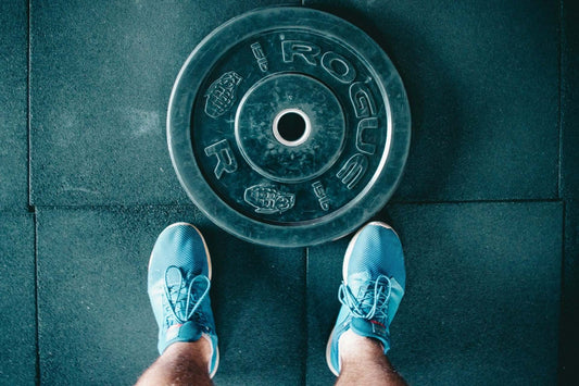 Person in blue sneakers standing near a weight plate on a gym floor