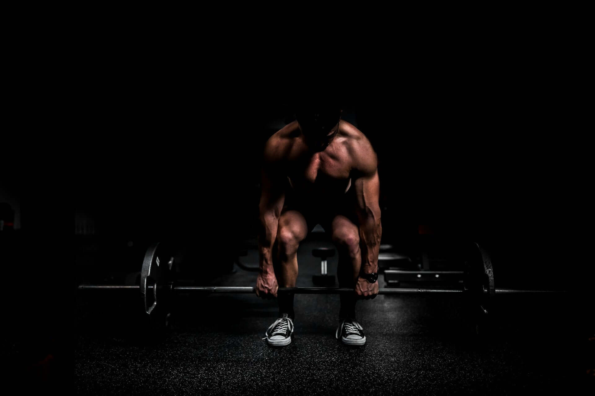 Man lifting barbell in dark gym, highlighting strength training benefits of creatine supplements.